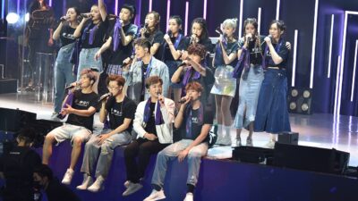 Performers on a lit concert stage before a crowd