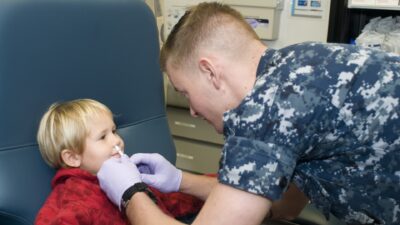 A Navy corpsman administers a nasal flu vaccine to a young child