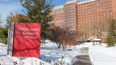 Red sign at the south entrance of the NIH Clinical Center, Building 10, in Bethesda, Maryland, with snow on the ground